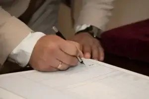 A man wearing a wedding ring signing a prenuptial agreement