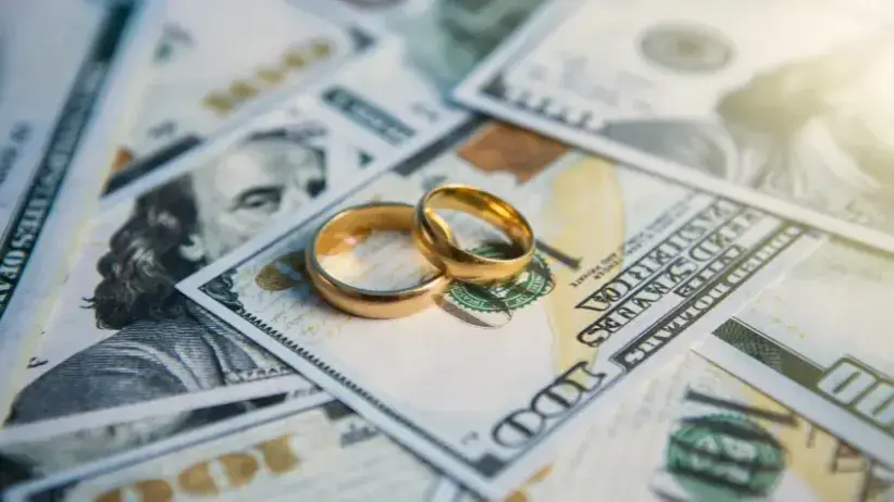 Wedding rings on top of 100 dollar bills representing financial disclosure